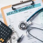Clipboard with Health Insurance papers, calculator, and stethoscope
