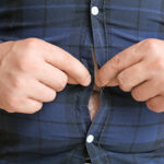 Overweight man trying to button his shirt