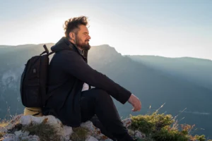Man with backpack sitting on top of a mountain