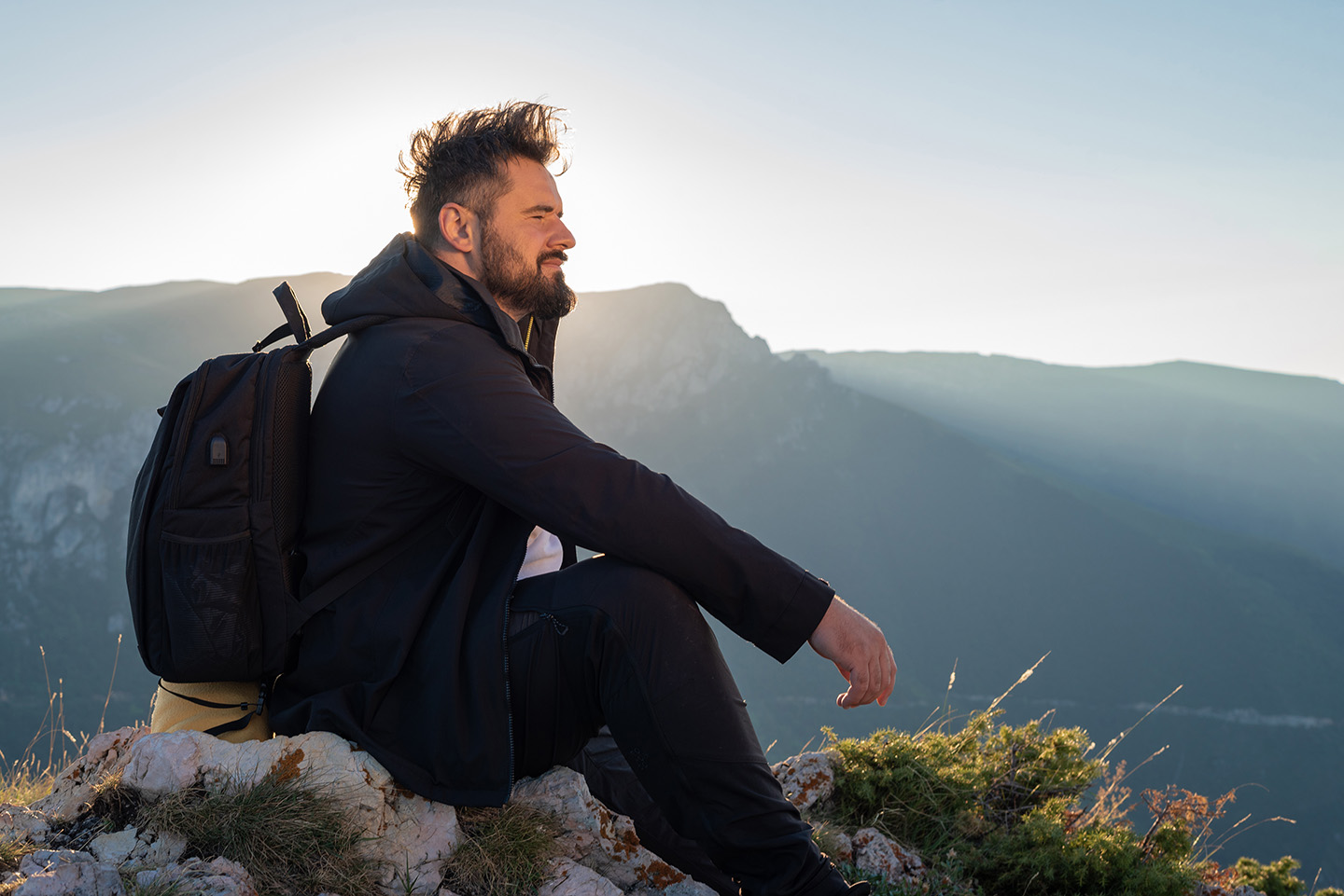 Man with backpack sitting on top of a mountain